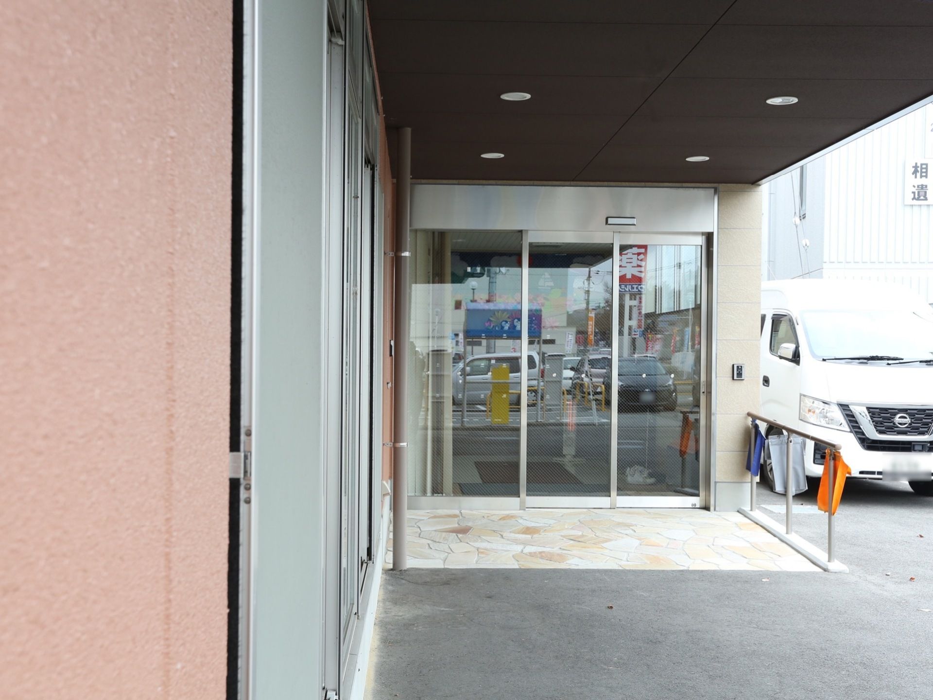 玄関は自動扉になっている。玄関前には手すりが設置され、新聞受けの袋がかかっている。すぐ横に車が停まっている。