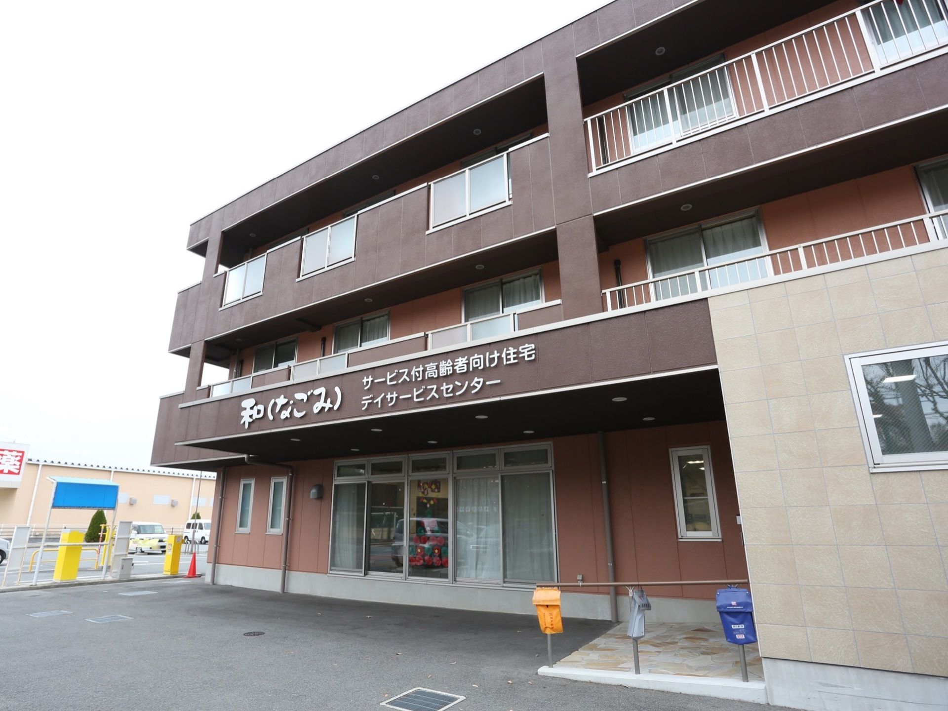 茶色系統の色を基調とした外壁の３階建ての施設である。玄関前はゆるやかなスロープになっていて、手すりが設置されている。