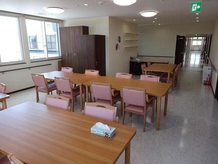 リビングには４人用の木製テーブルセットが並べられていて、ピンクの椅子がアクセントになっている。壁沿いは全て手すりがあり、移動を助けてくれる。