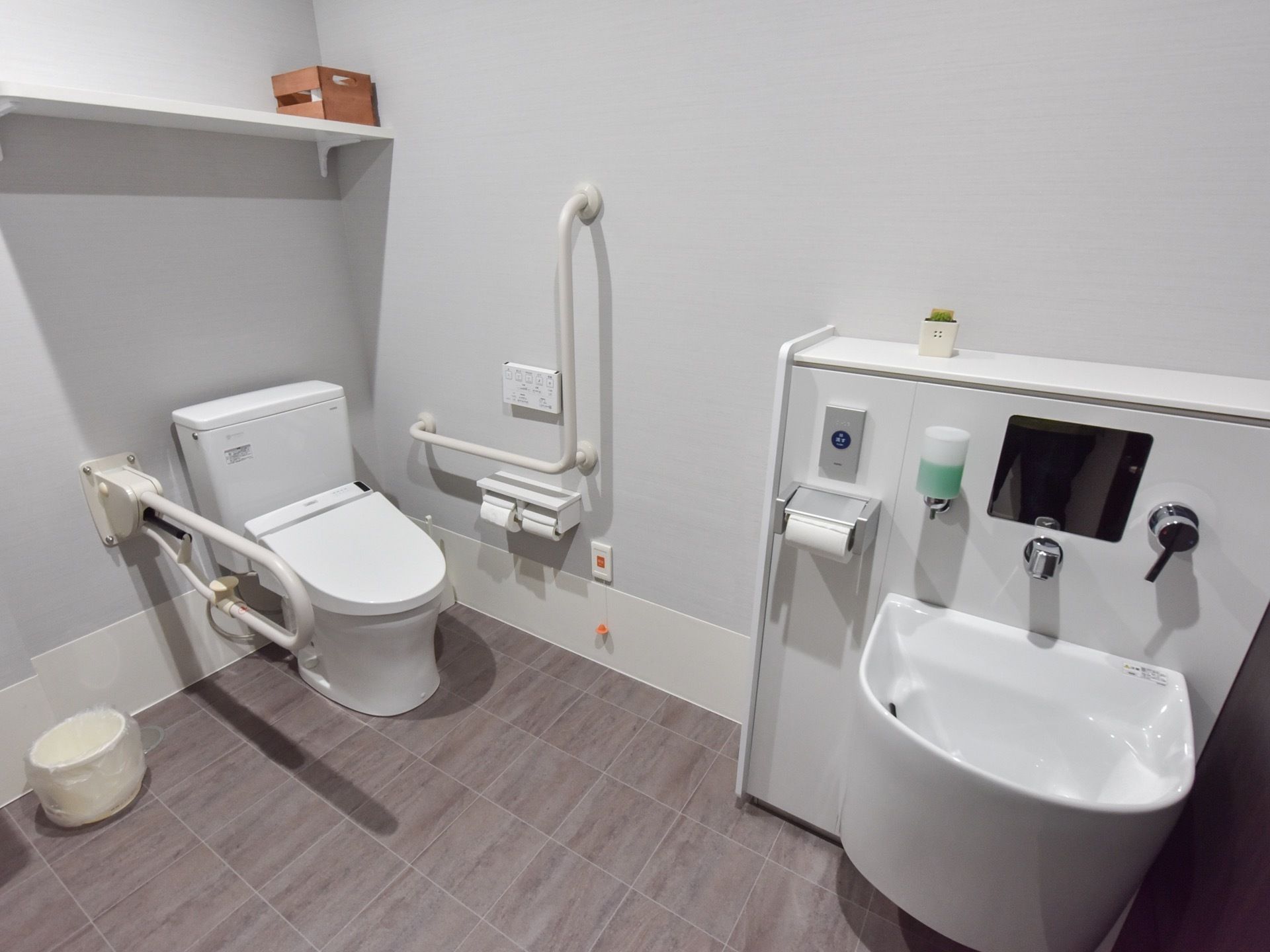 トイレの左奥に、温水洗浄便座付きトイレがある。壁に操作盤や手すりが付いている。右手にオストメイト用のトイレがある。