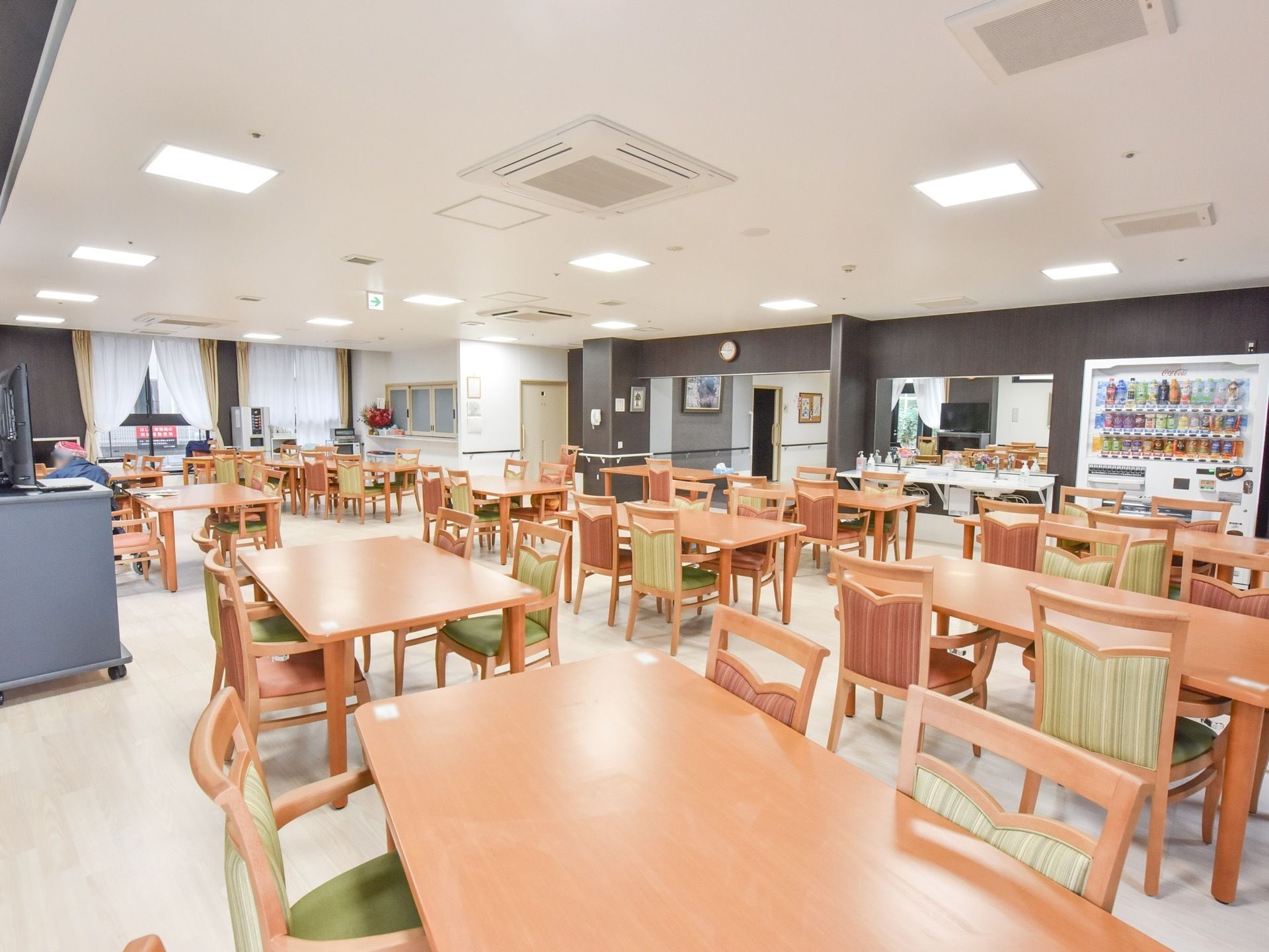 広い室内に、揃いのテーブルセットがたくさん設置されている。右手に手洗い場があり、その隣に自動販売機がある。