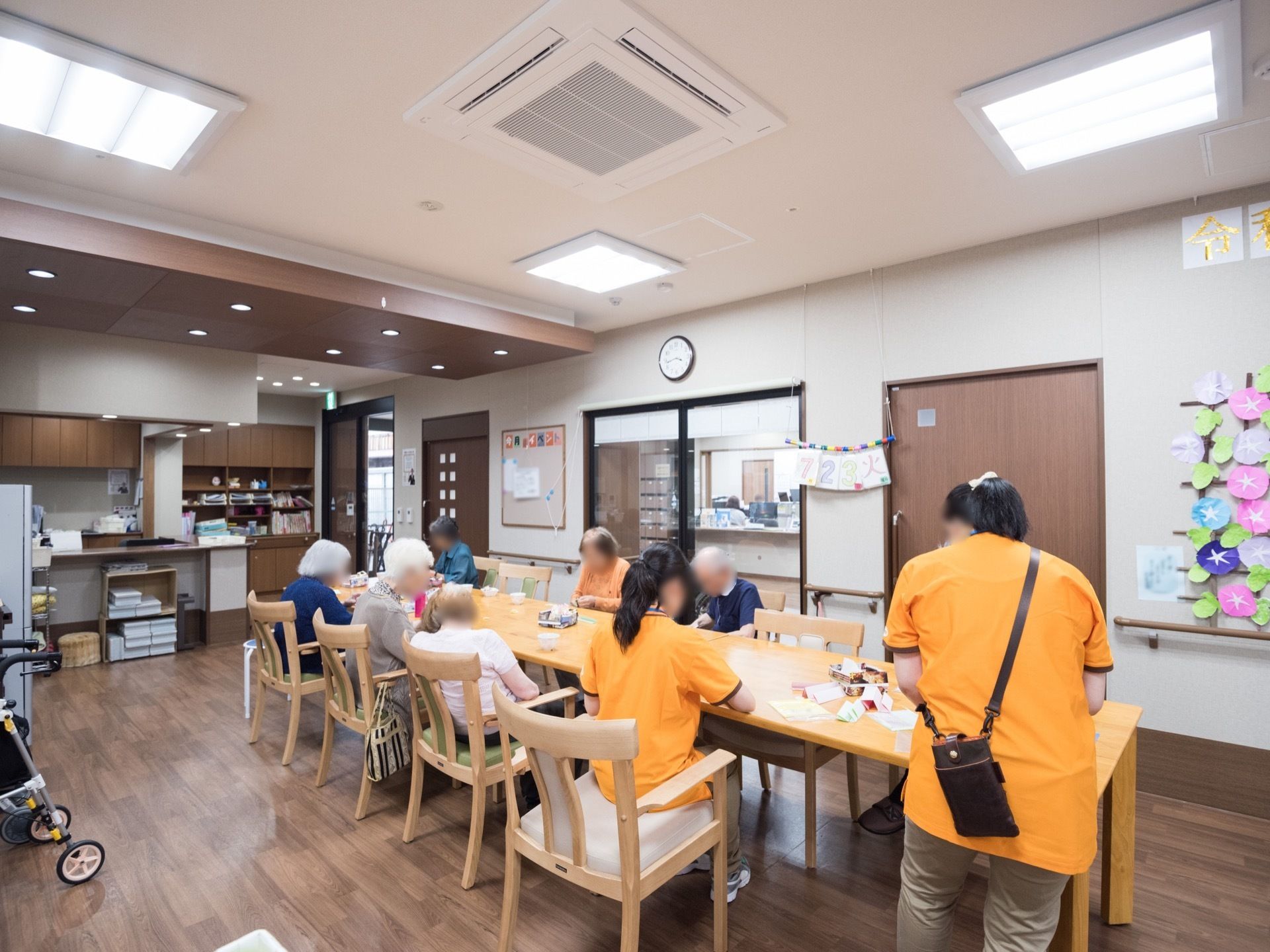 テーブルを並べた共有スペース。入居者様とスタッフが椅子を並べて、お茶を飲んだり、作業をしたりしている。