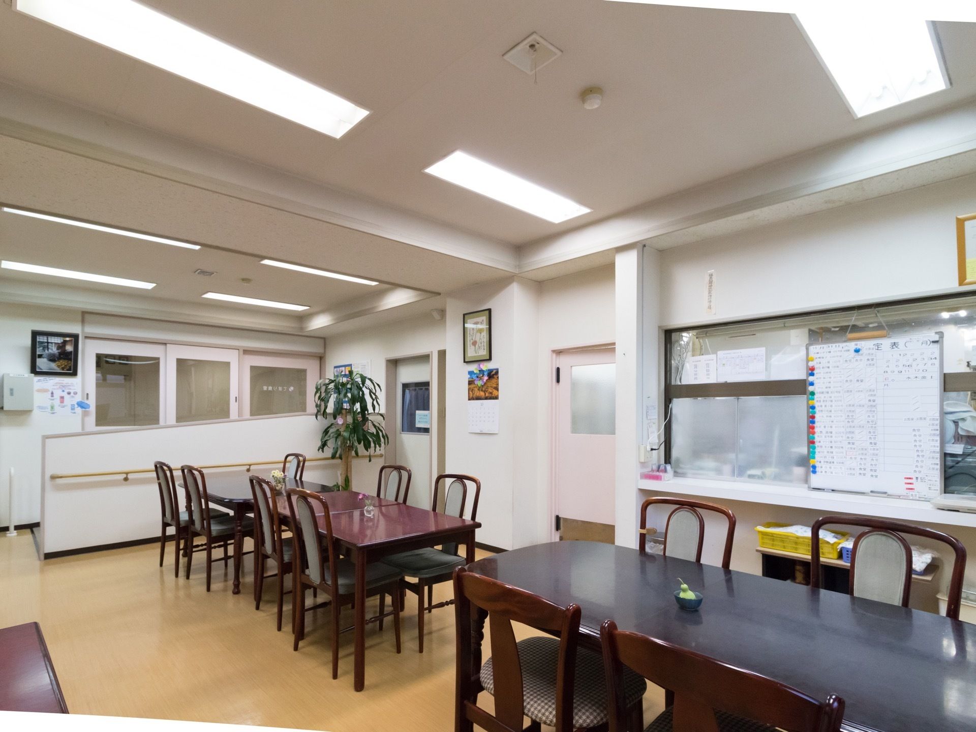 ダークブラウンのダイニングテーブルが並んでいる。部屋の奥の壁に手すりが設置されており、近くに観葉植物が置かれている。