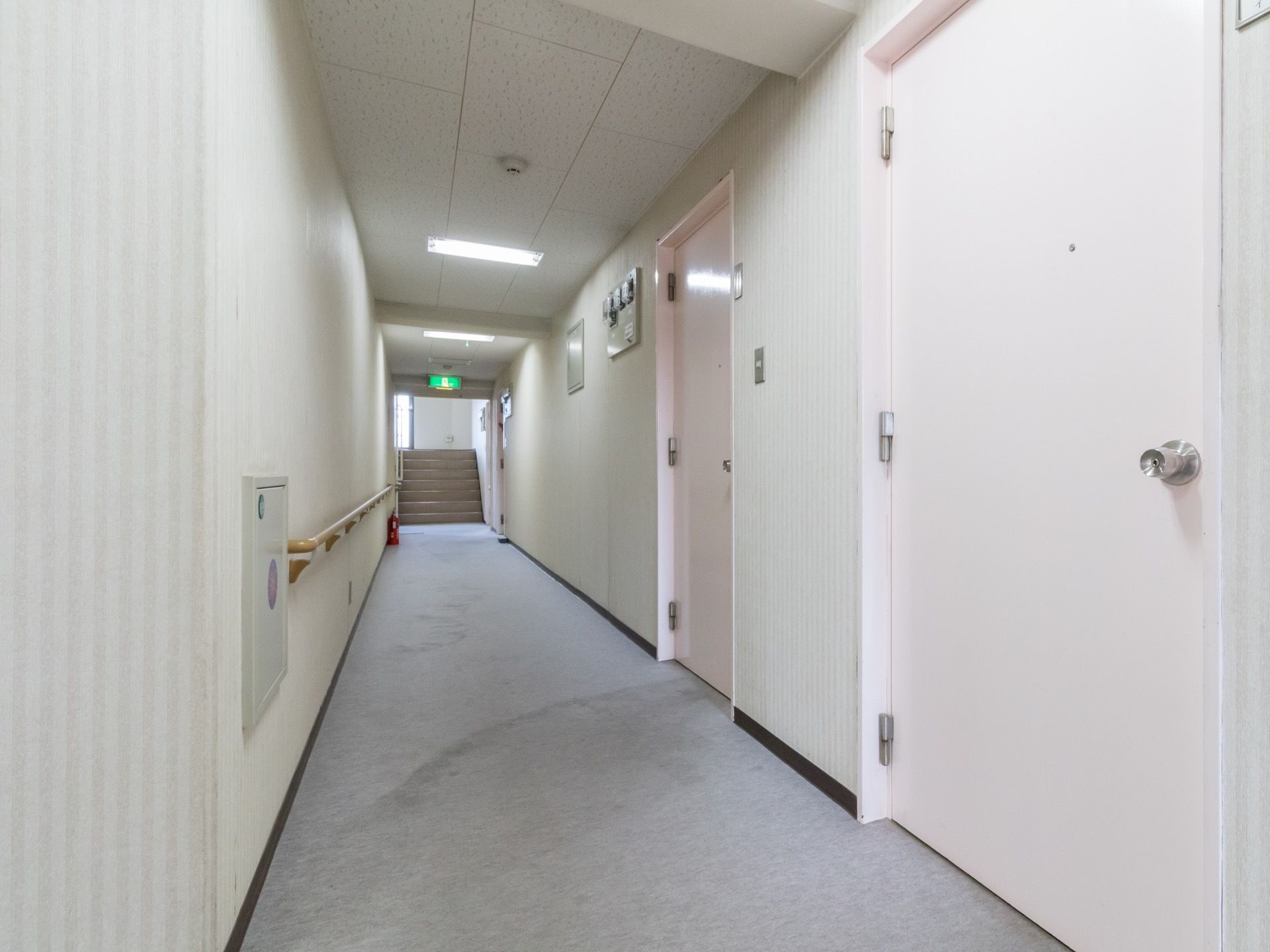 ベージュとホワイトのストライプの壁にピンクのドアが設置されている明るい雰囲気の廊下には手すりが設置されている。