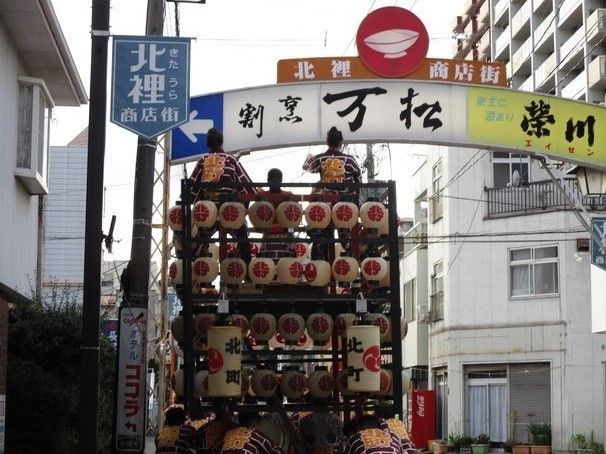 近隣にある北裡商店街で祭りが開催されている様子。ハッピを着た人々が提灯のついた屋台を押しながら進んでいる。
