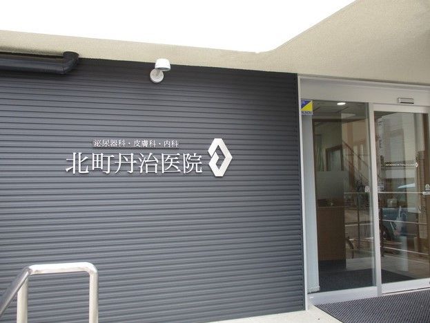 黒い壁に白い文字で病院名が掲げられている。落ち着いたモダンな雰囲気。泌尿器科、皮膚科、内科の診療を行なっている。