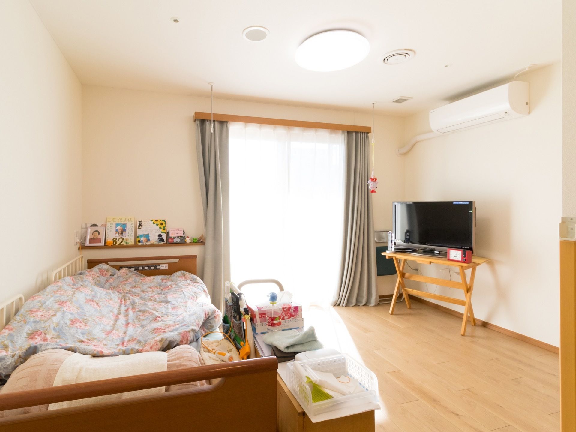 居室には、掃き出し窓・エアコンが備え付けられている。ベッドの枕元にはナースコールが置かれ、足元の壁には飾り棚が作り付けられている。