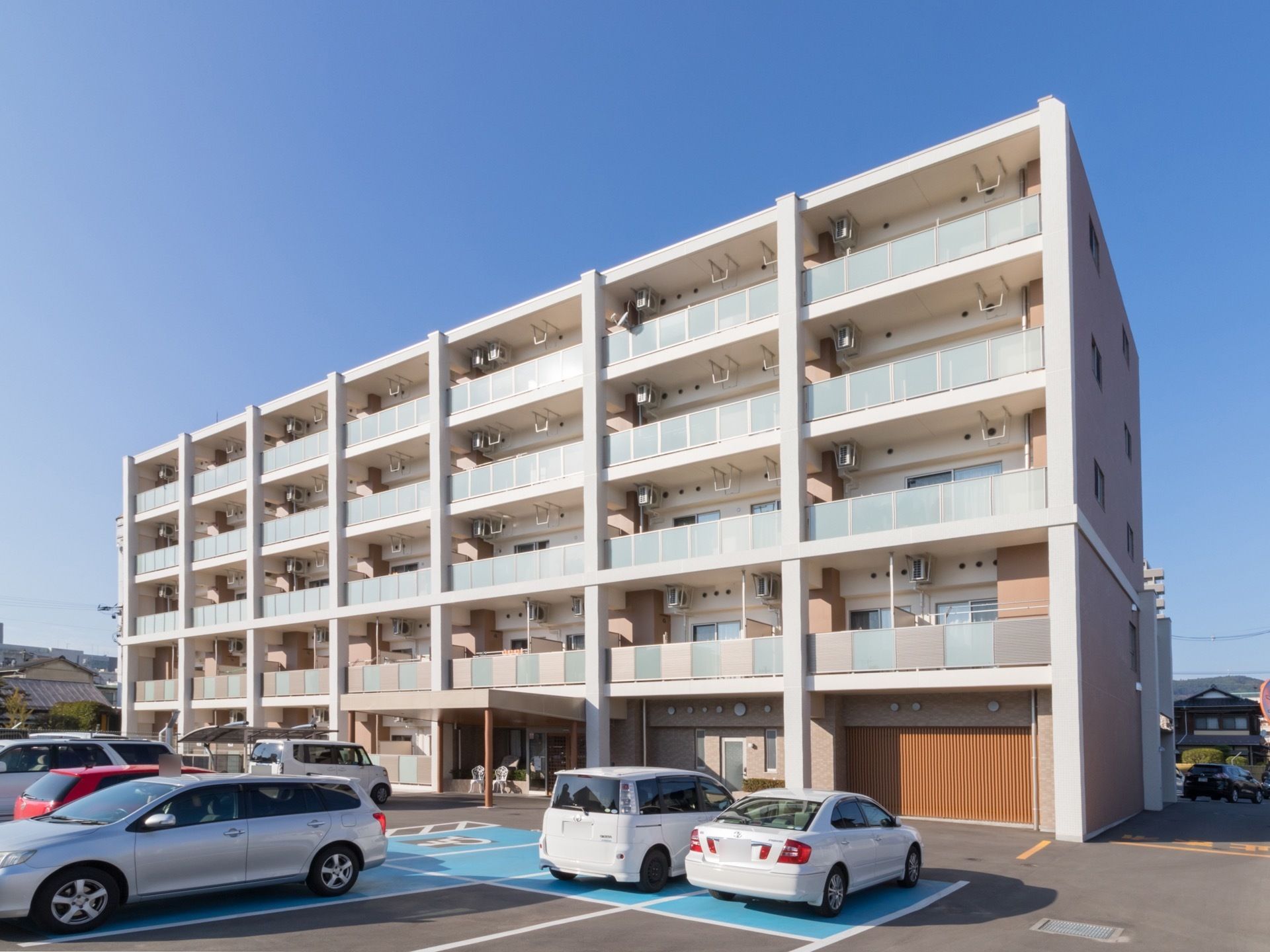 パステルカラーが使われた５階建ての、マンションのような建物。建物の前には、広い駐車場があり、車椅子専用のスペースも充実している。