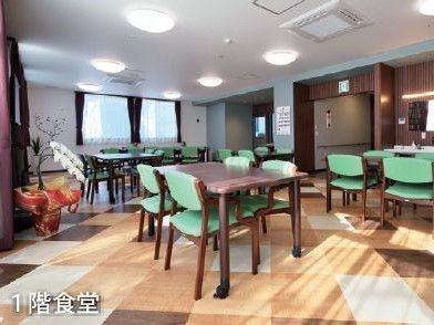 窓からの光と天井の照明が調和して明るく落ち着ける空間である。入居者様がゆったりと行き来できるように配慮したテーブルセットの配置である。