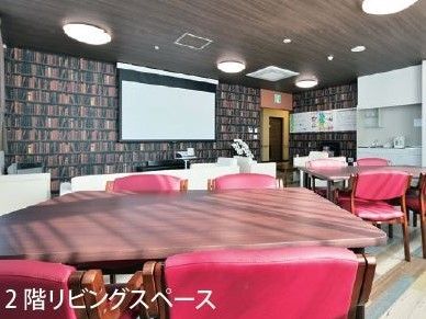 ゆったりと置かれたテーブルセットの椅子は赤く、給湯設備もある。木材で美しくデザインされた壁にはスクリーンが設置されている。