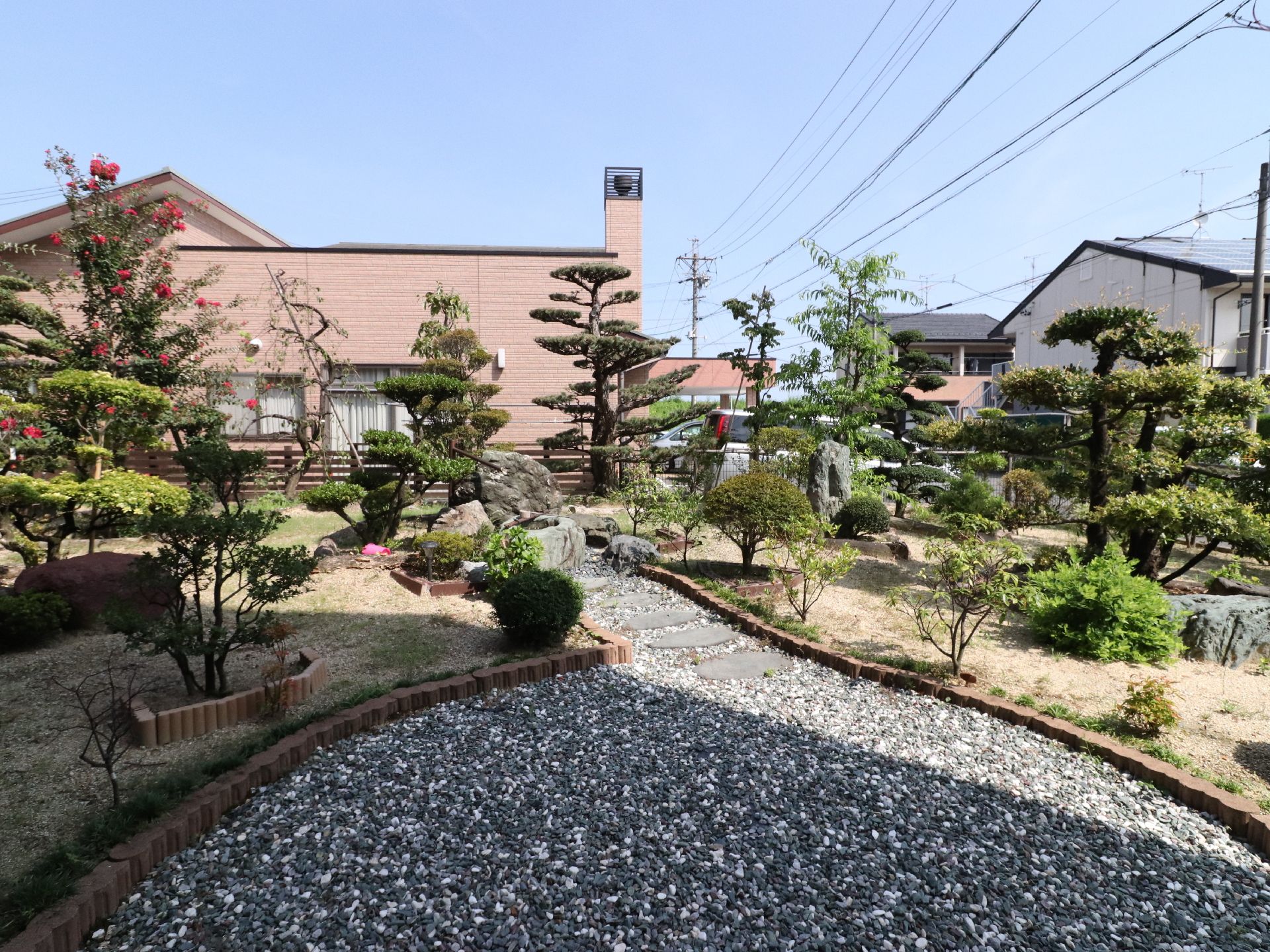 木製のフェンスで囲まれた庭がある。芝生が一部に敷いてある。砂利と煉瓦で様々な木々をかこっている。巨石が所々に置いてある。