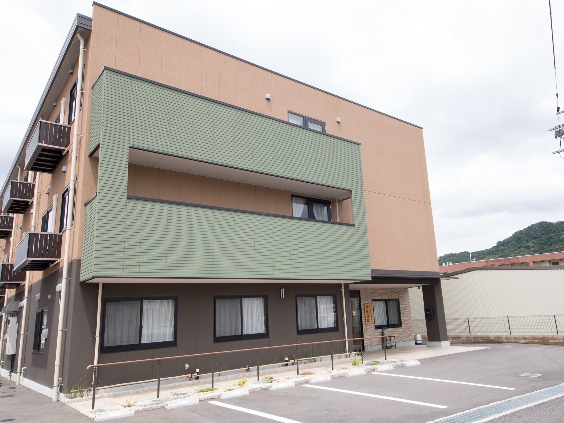 施設の建物は３階建てで、落ち着いたグリーンとブラウン、ベージュを組み合わせた外壁がモダンな雰囲気である。