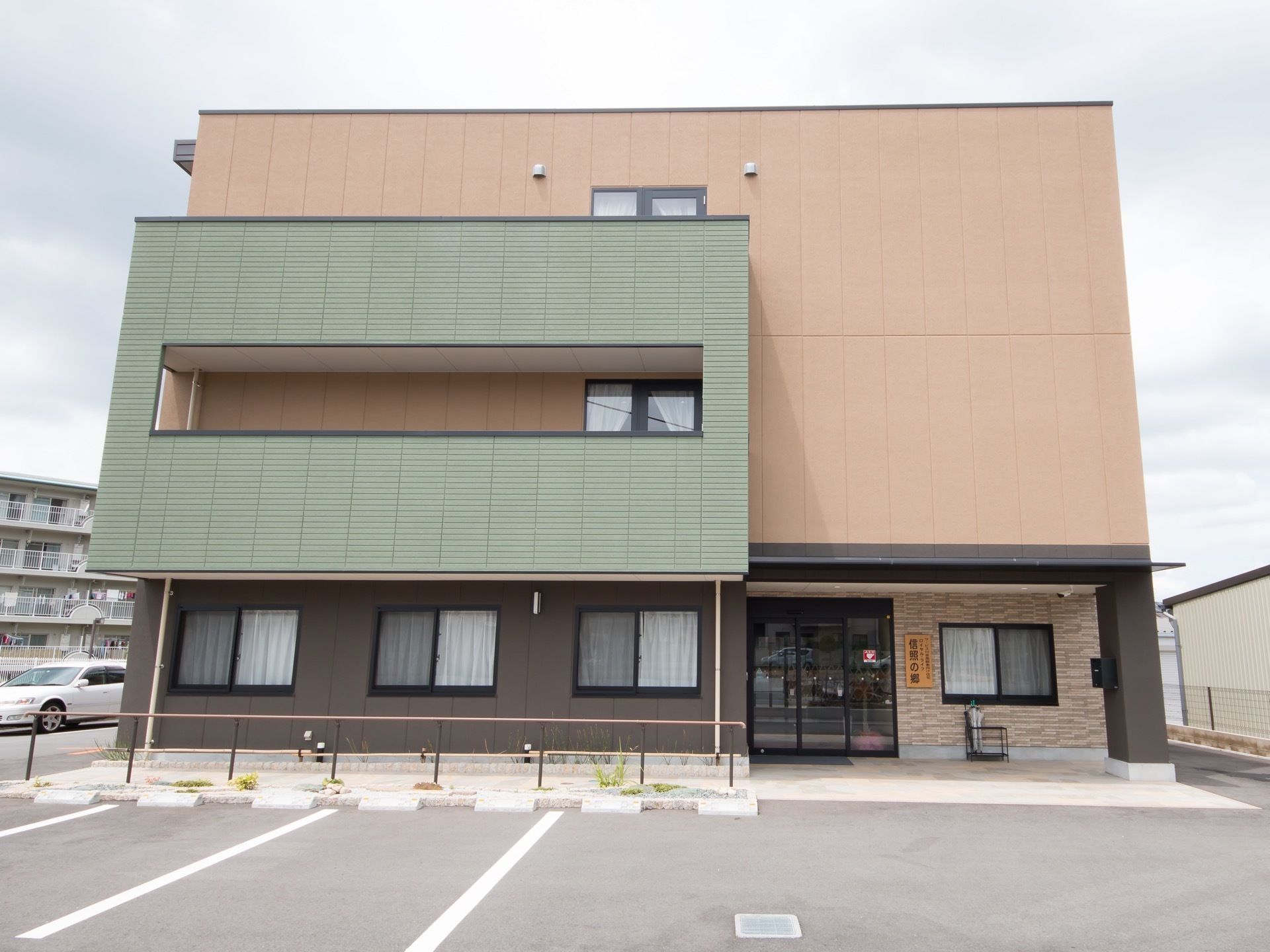 建物の前には広いスペースがあり、駐車場となっている。入り口の横は通路になっていて、手すりが設置されている。