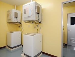 洗濯パンの上に縦型全自動洗濯機が置かれている。その上に手前に扉がある衣類乾燥機が壁に掛けられている。