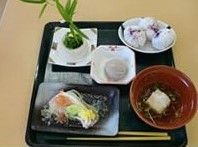黒いお膳に食事が用意されている。右手前の赤いお椀にぜんざいがある。左手前には四角い平皿に料理が盛られ、中央と奥左右に小鉢がある。