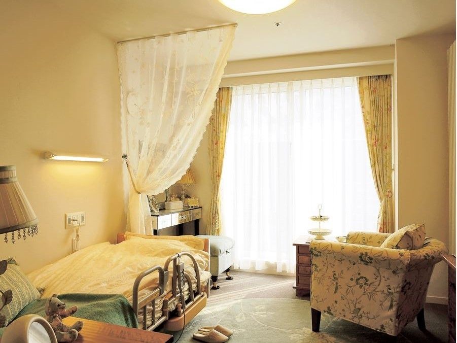 大きな窓のある、明るい部屋である。洗練された家具が置いてあり、きれいな空間である。ベッドのそばには照明とコンセントが備え付けられている。