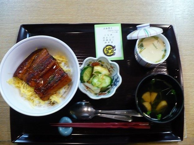 黒いトレーの上に、うな丼と茶わん蒸し、お吸い物と漬物が置かれている。また、メニュー表も用意されている。