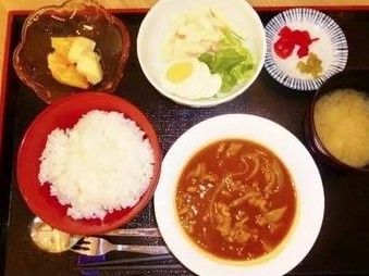 食事のメニューの一例である。膳の上に、ご飯、カレー、野菜、漬け物、フルーツ、汁物のお椀が置かれている。