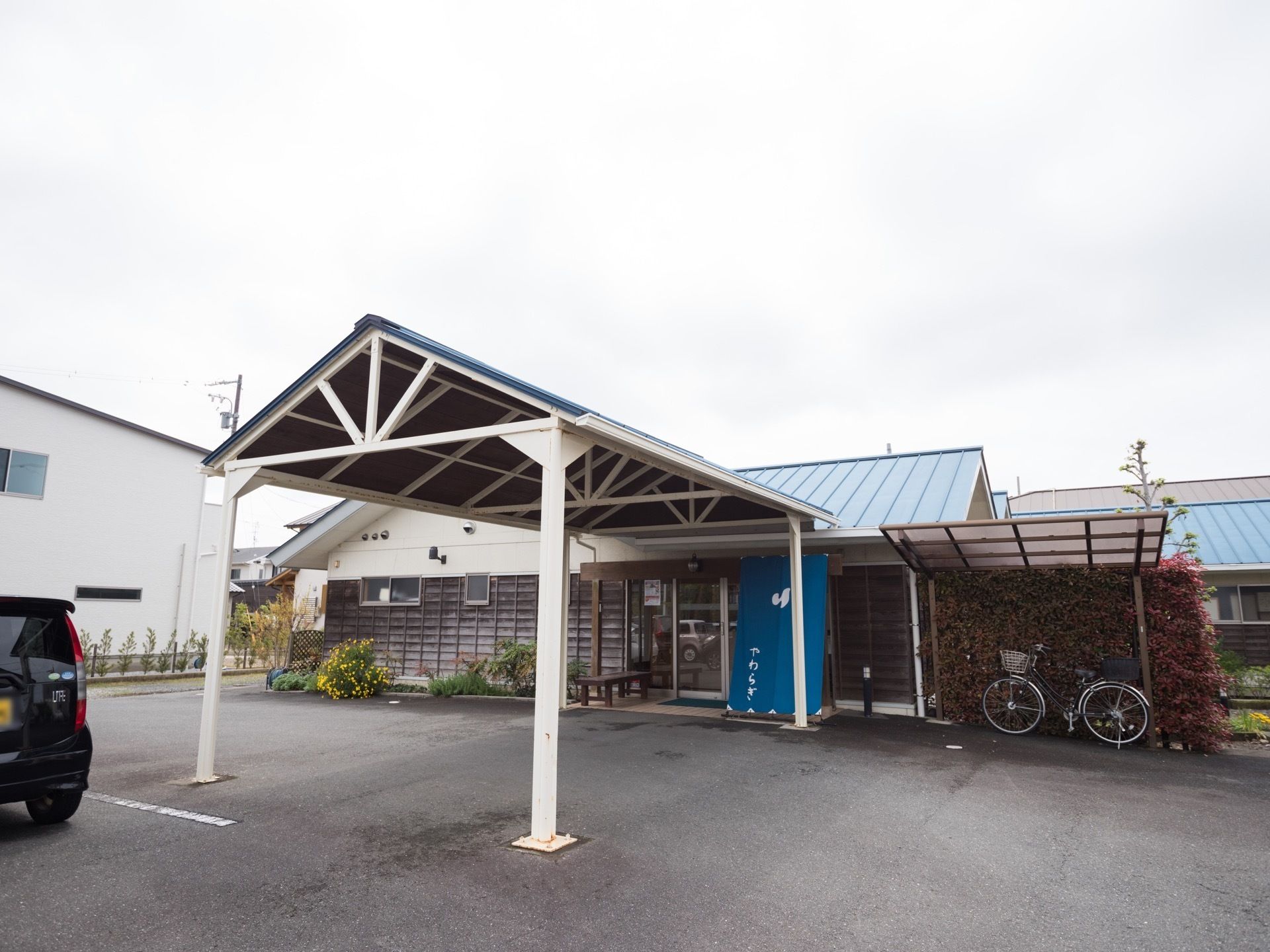 施設の玄関の前には、三角の屋根の長いひさしが設置されている。玄関の右側には自転車置き場があり、左側には花壇がある。
