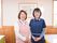 親しみやすい雰囲気がある二人の女性スタッフがにこやかに立っている。後ろの壁には絵が飾られていて、側にペンダントライトが吊るされている。