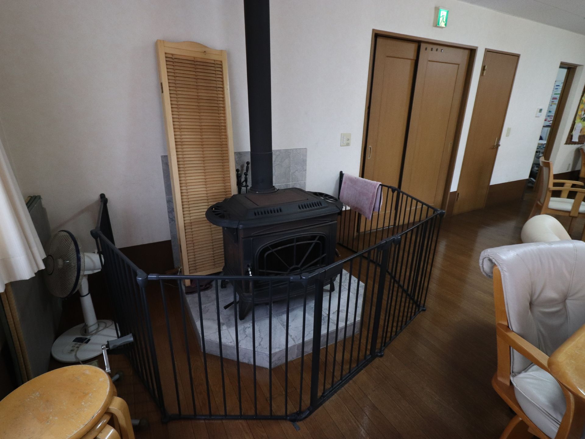 扇風機が一台置いてある。スツールが数脚積み重ねてある。大理石の台のうえに、暖炉があり、鉄のフェンスで囲まれている。