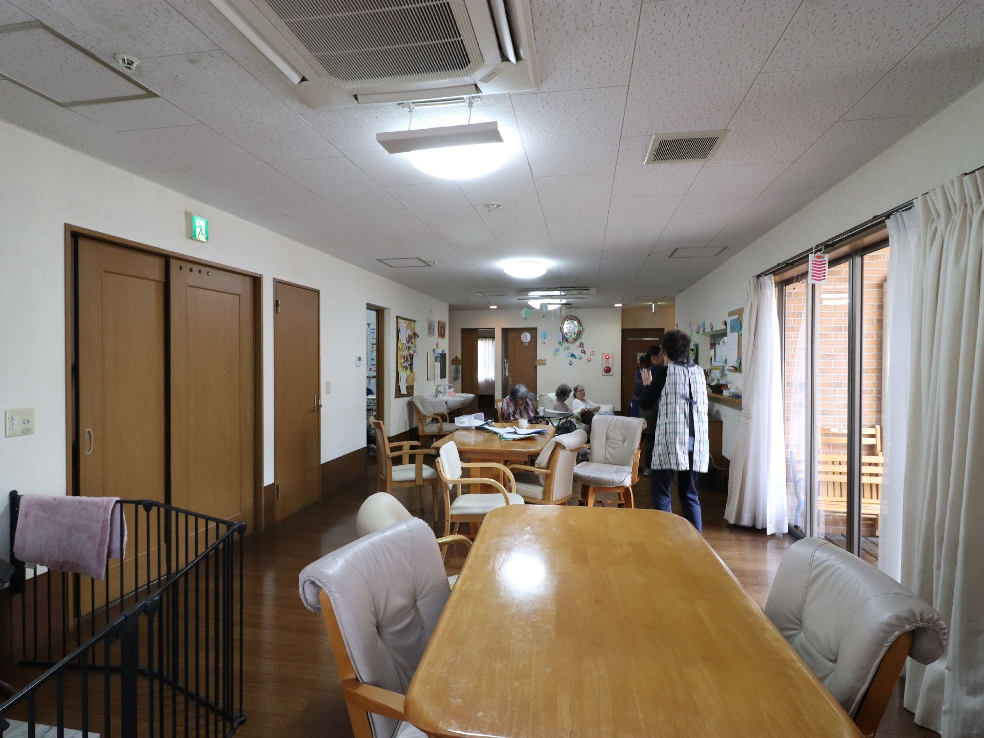 窓にかかったカーテンは開いていて、カーテンレールには虫よけグッズがぶら下がっている。茶色いテーブルの周りには椅子がある。