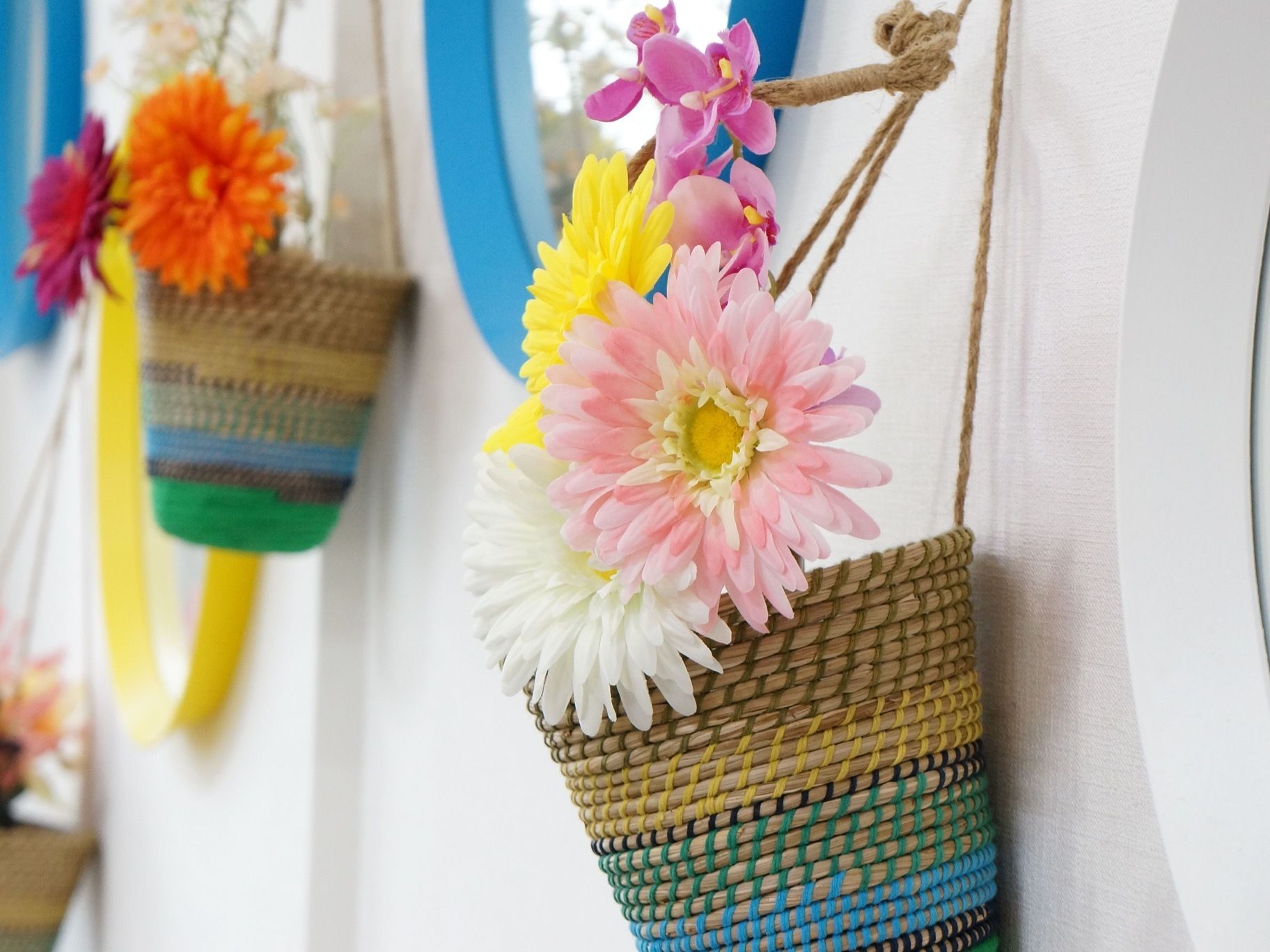 カゴの中に、カラフルな造花が入ったものが、壁からいくつもぶら下がっている。丸い色の付いた鏡のようなものも壁にある。