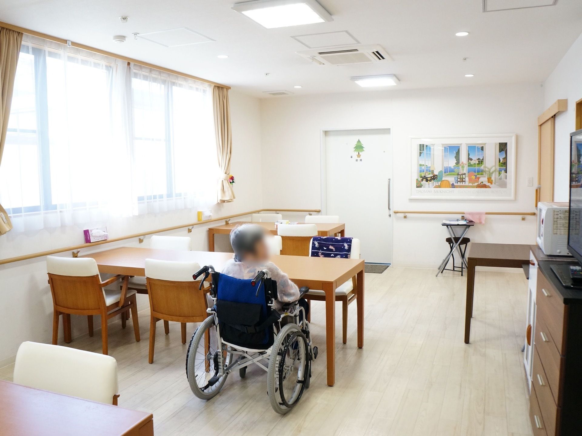 長方形の机が壁に接して配置されている。机の近くには窓があり、カーテンが掛けられている。奥の壁にはが絵入りの額縁が飾られている。