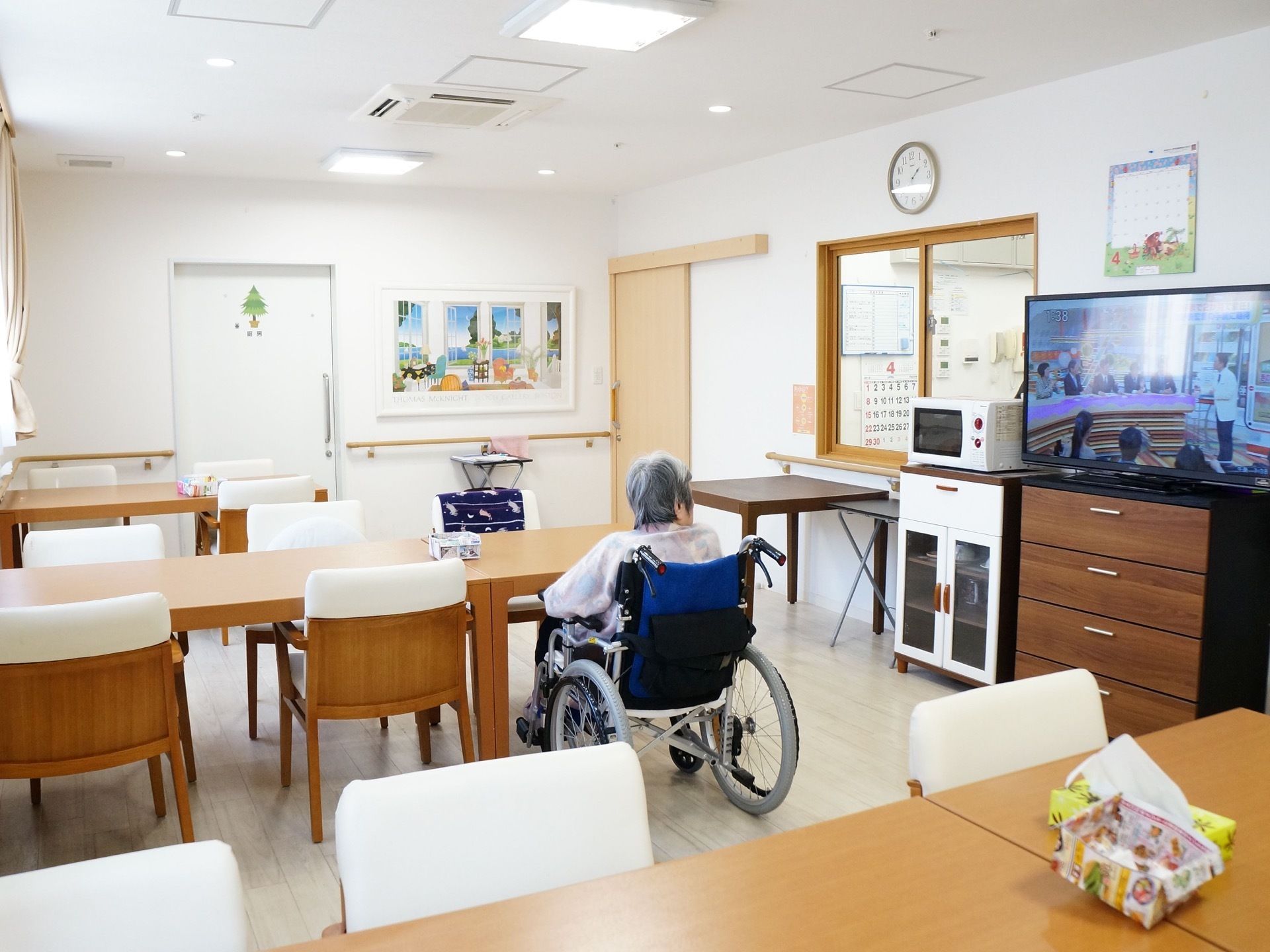 室内に長机と椅子が配置されている。机と椅子はともに木製で、同じ材質のようにみえる。部屋の右側には家電製品が設置されている。