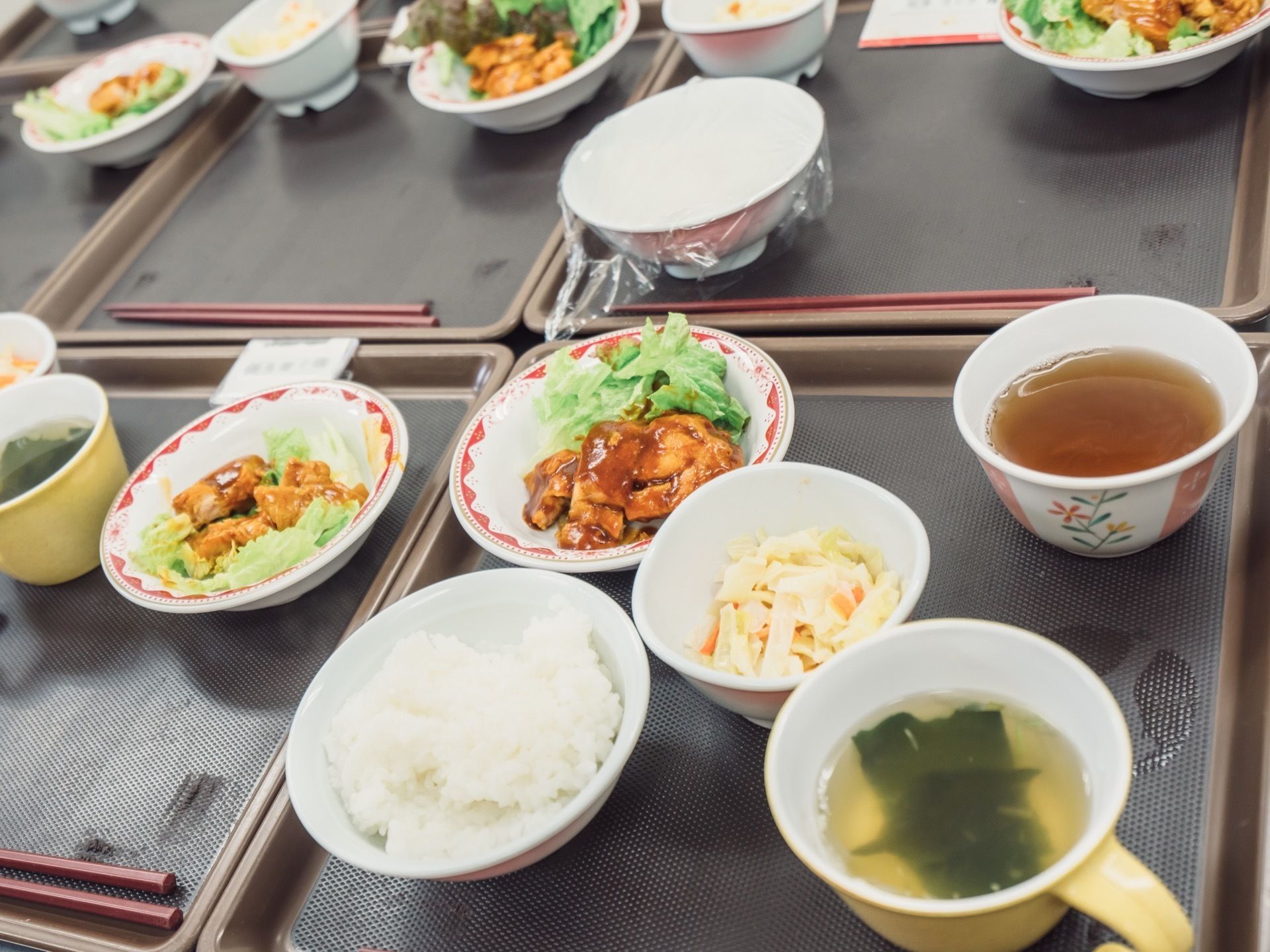 お盆に上にはご飯と味噌汁、主菜のおかずとその他に副菜が二つ用意されている。味噌汁の容器には取っ手がついている。
