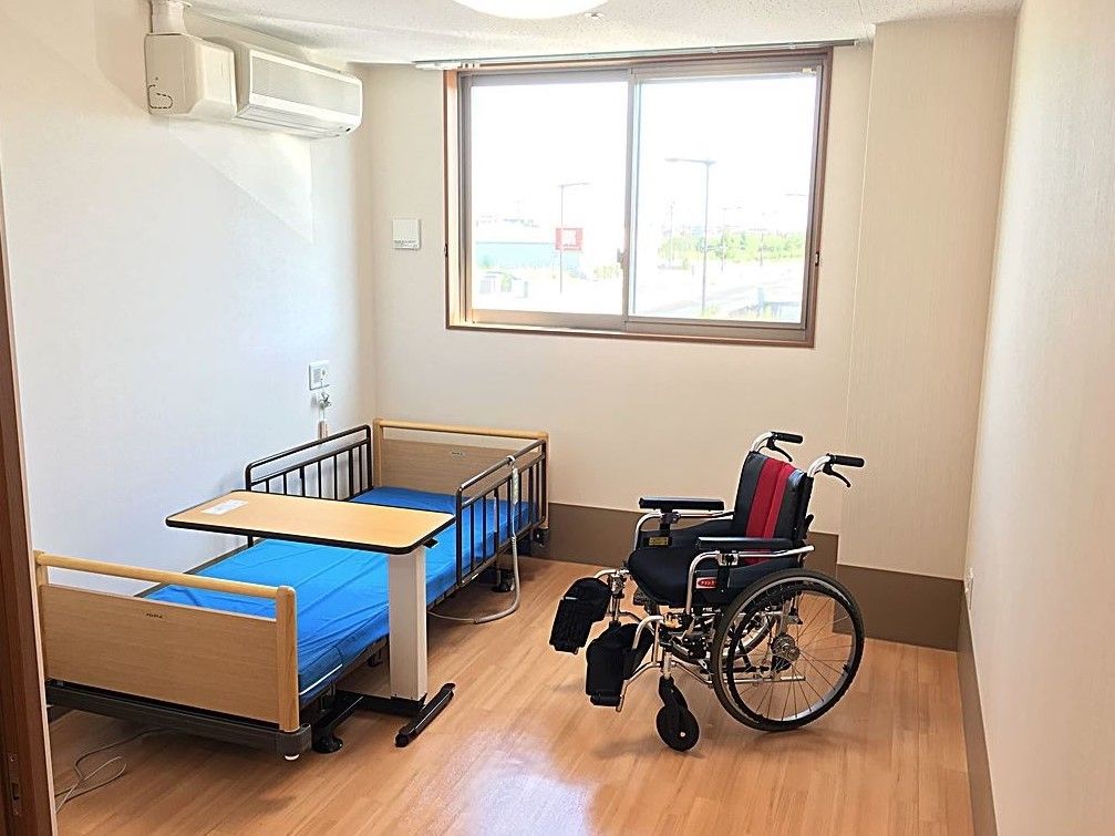 木目調の床を取り入れた、ぬくもりを感じられる居室である。介護用ベッドの傍の壁にナースコールを設置している。