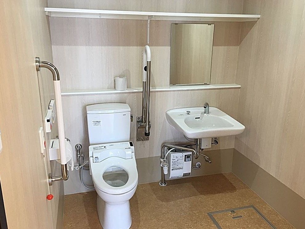 広々としたトイレスペースである。便座の両側に手すりを備え、左側は可動式で使用しない時は上にあげておくことができる。