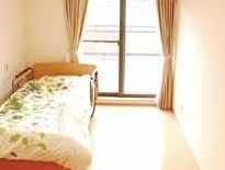 部屋の一辺に寄せて配置された緑の蔦柄の布団を伸せたベッド