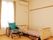 白い壁で大きな窓のある部屋に、低いベッドと緑色の車椅子が置かれている。窓からはやわらかな陽が差し込んでいる。