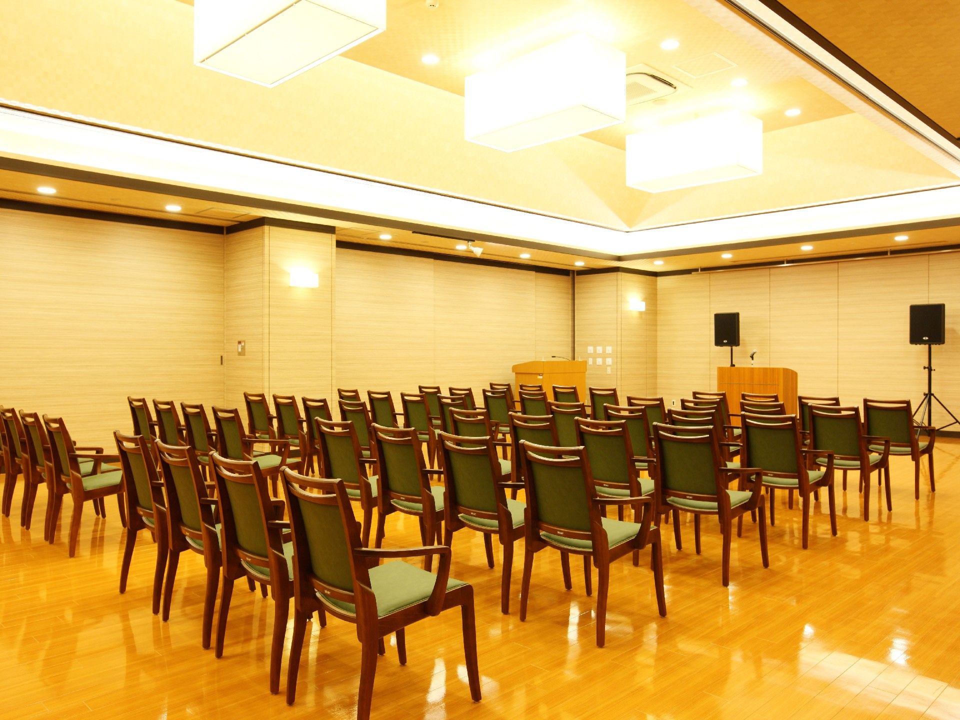 正面にマイクがのった演台があり、脇には司会者用の台もある。演壇の後ろにはスピーカーも置いてある。正面に向けて、多くの肘付き椅子が並んでいる。