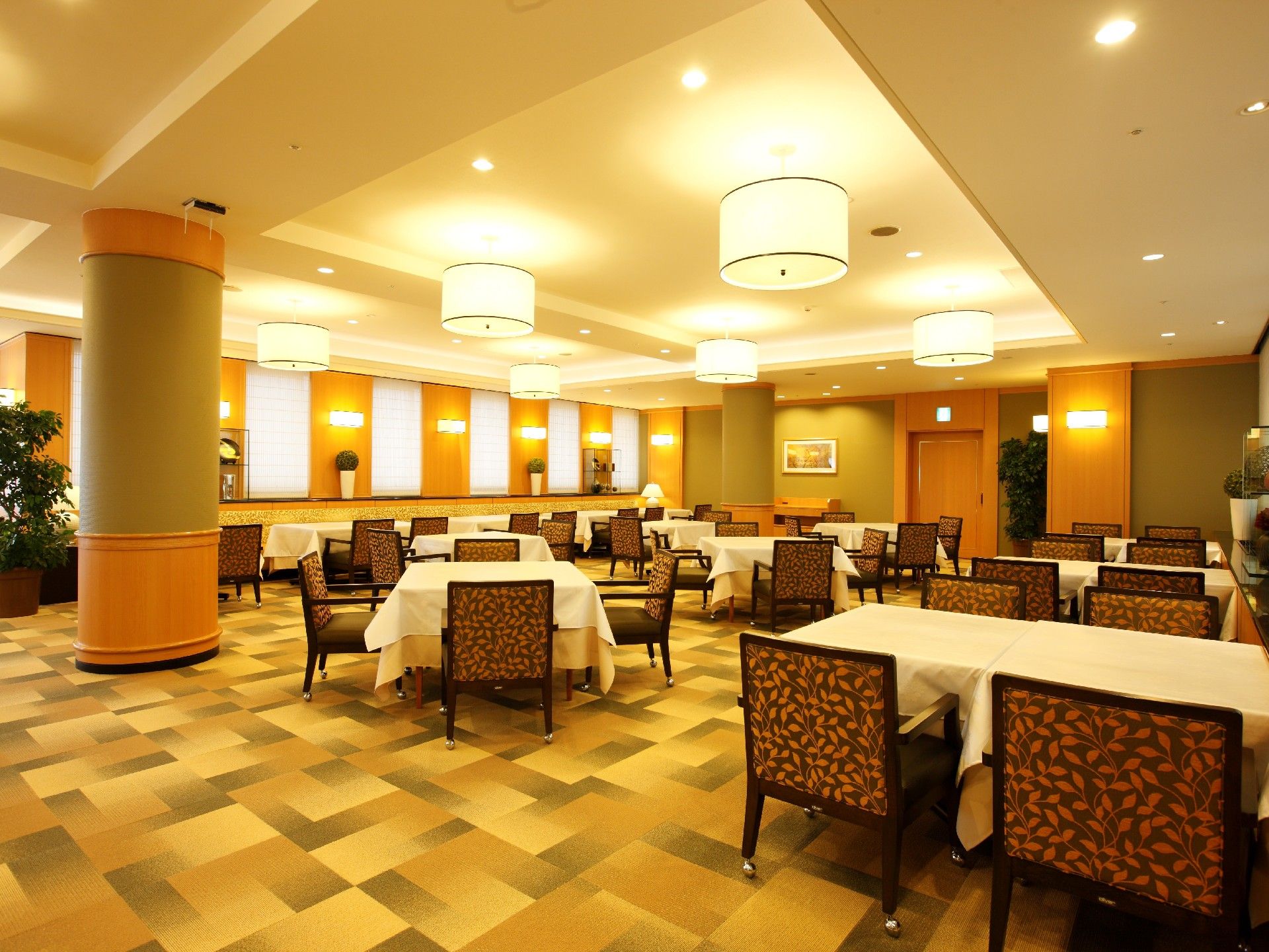 白いテーブルクロスをかけた４人掛けのテーブルが並ぶダイニング