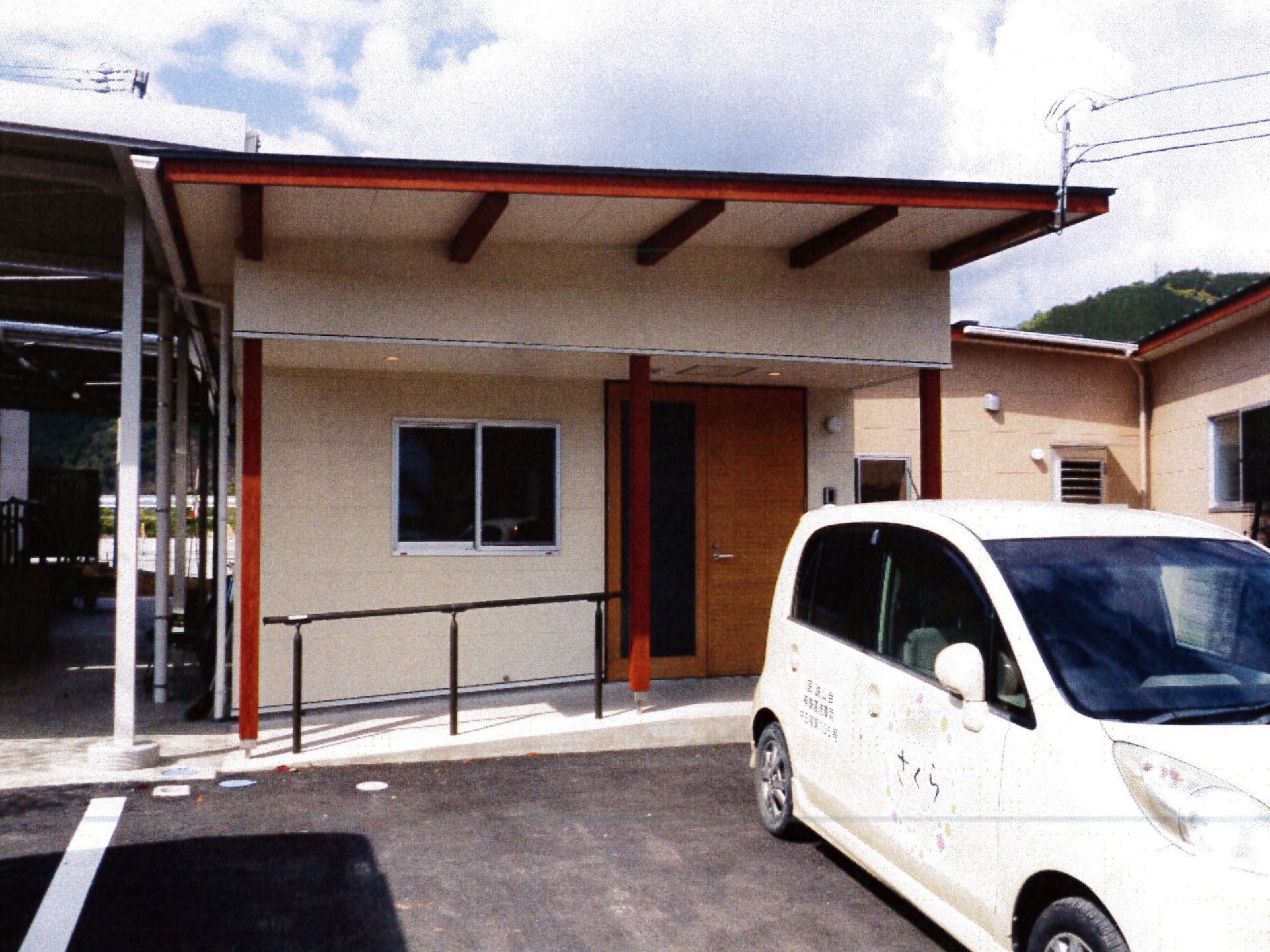 柱の赤みが差し色になったクリーム色の平屋建築の玄関口