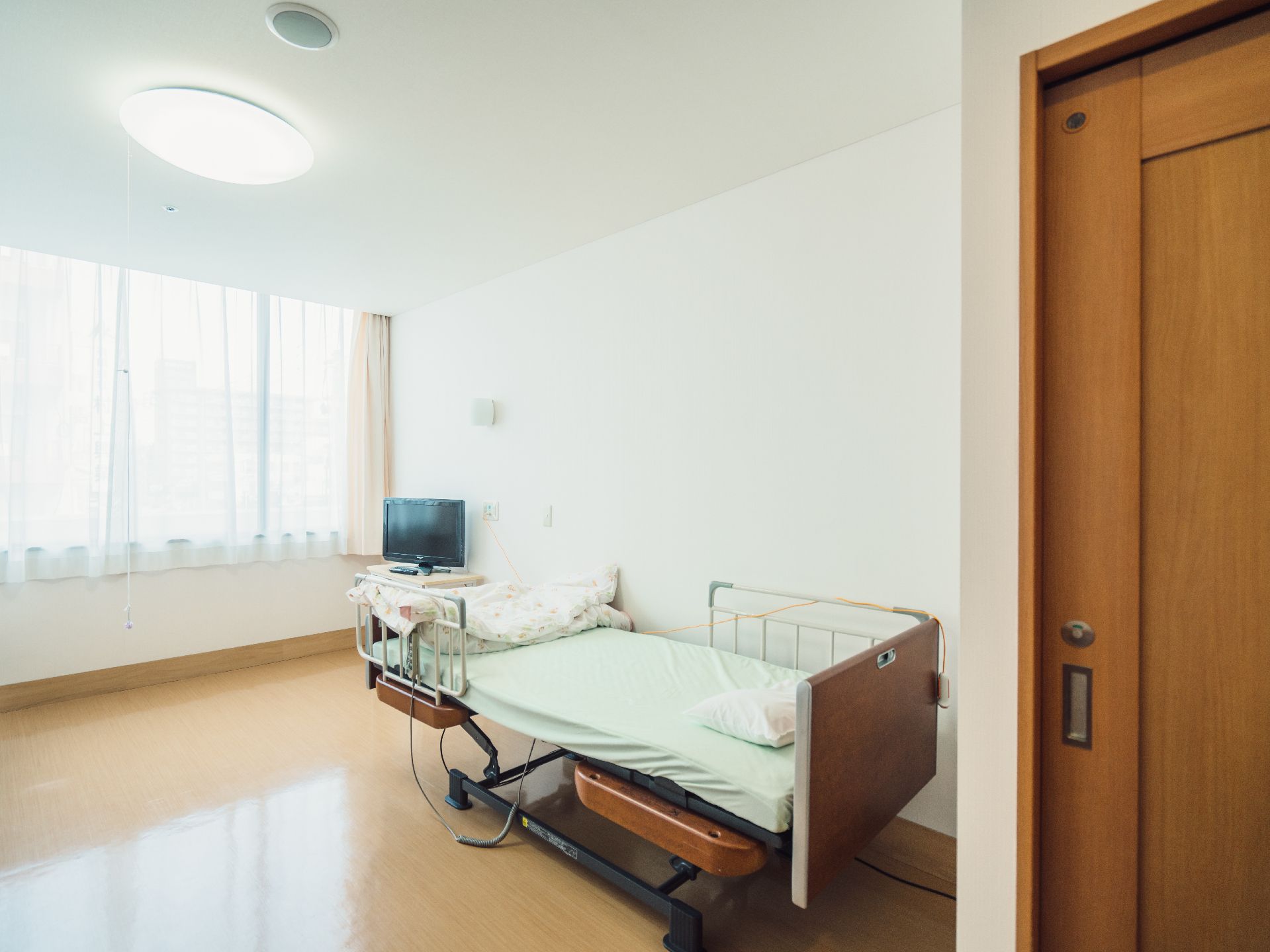 介護機能付きのベッドと小さなテレビが置かれた明るい部屋