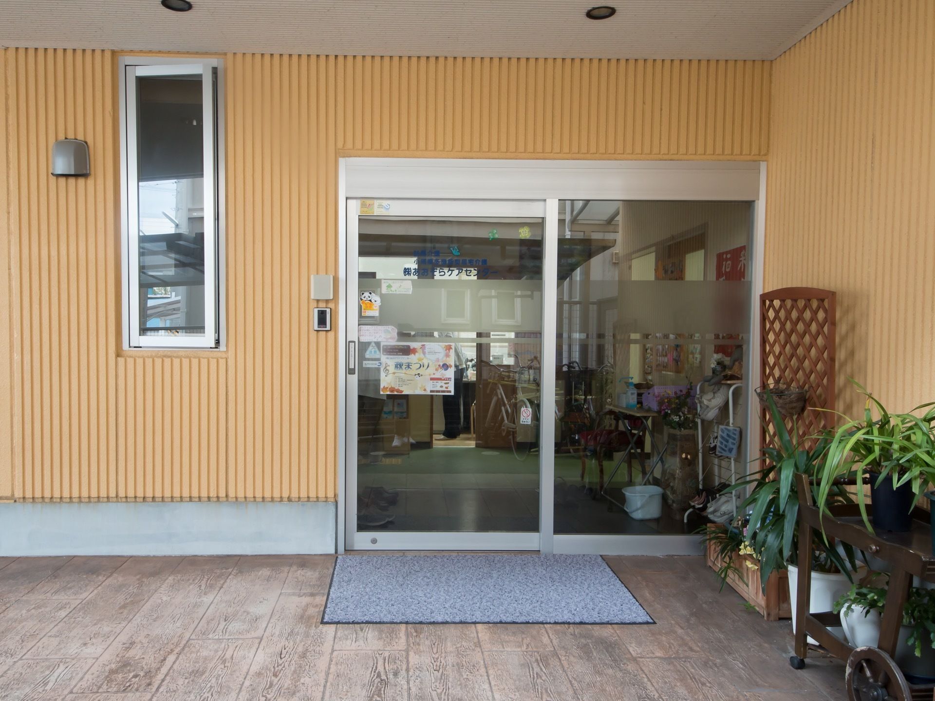 施設の玄関口を外から見たところ。すぐ横には植物の植えられたプランターが飾ってある。天井には照明が埋め込んである。