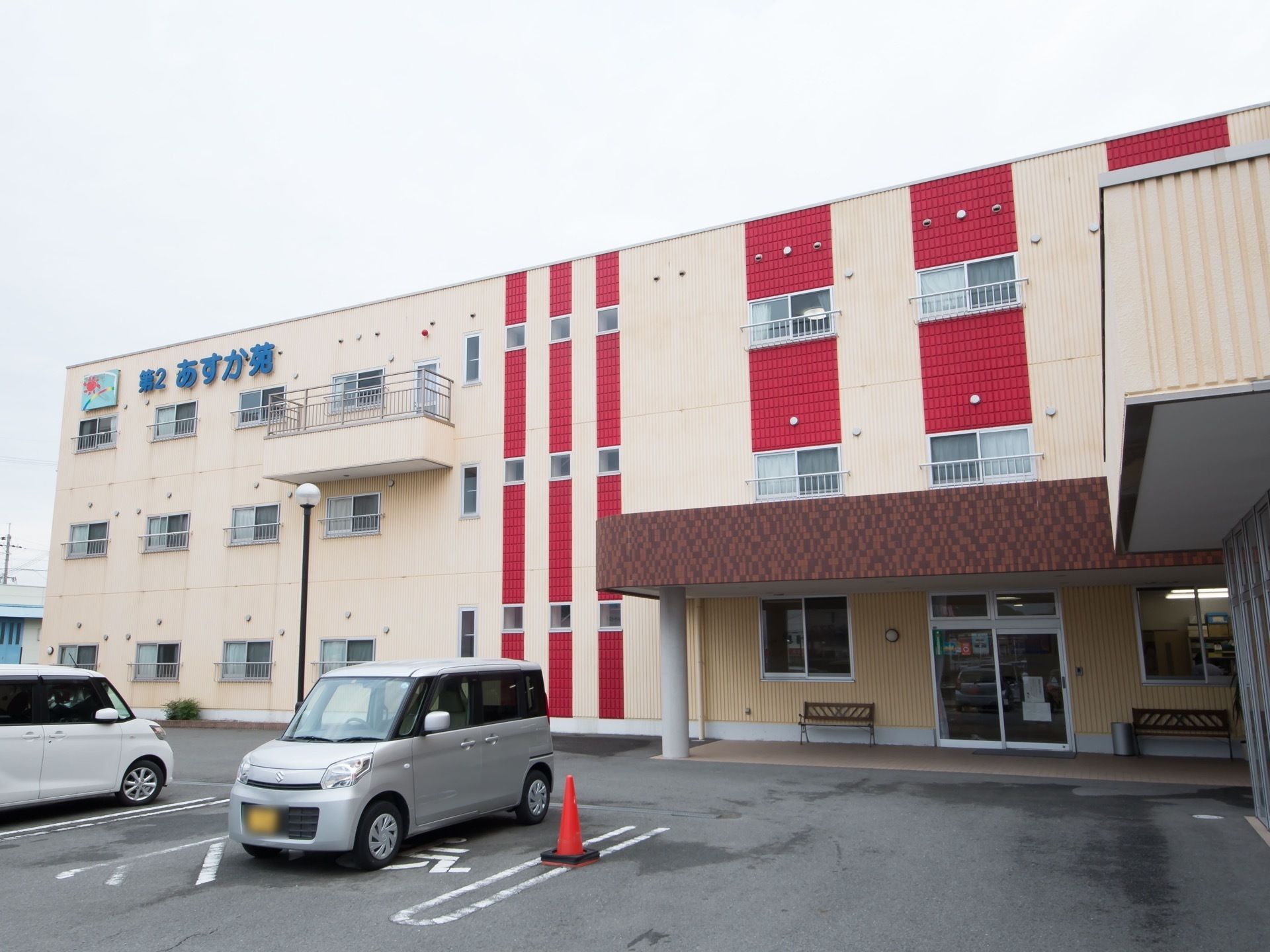 白い外壁に赤いラインが印象的な３階建ての施設である。さまざまな料金プランを取り揃え、質の高い介護サービスを提供している。