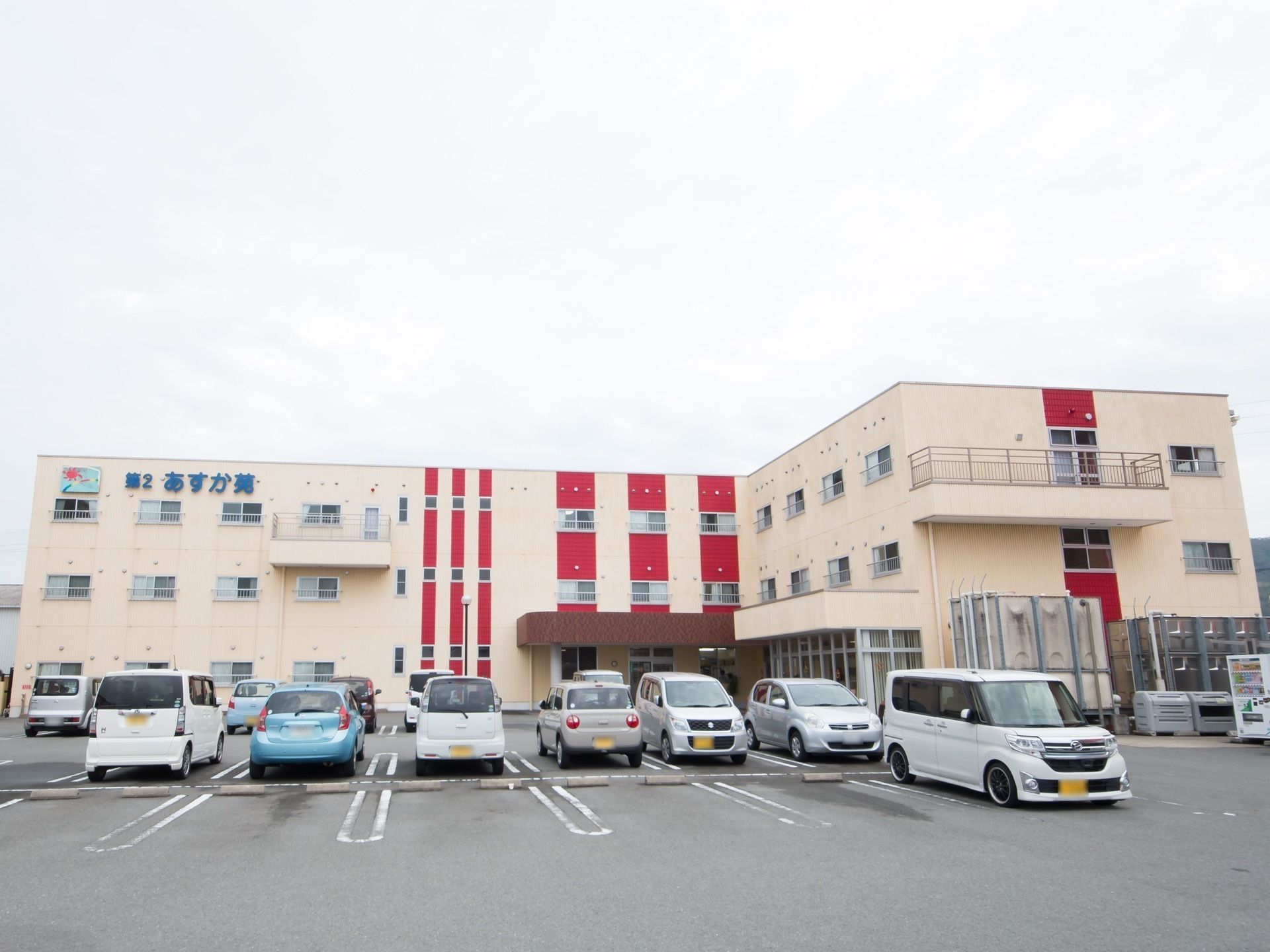 クリーム色の外壁に赤いラインの装飾が入った３階建ての建物
