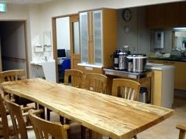 キッチンとリビングの間に食器棚が置かれている。食器棚の隣にはステンレスの台があり、大きな炊飯器がある。部屋の隅にはコンパクトな洗面台がある。