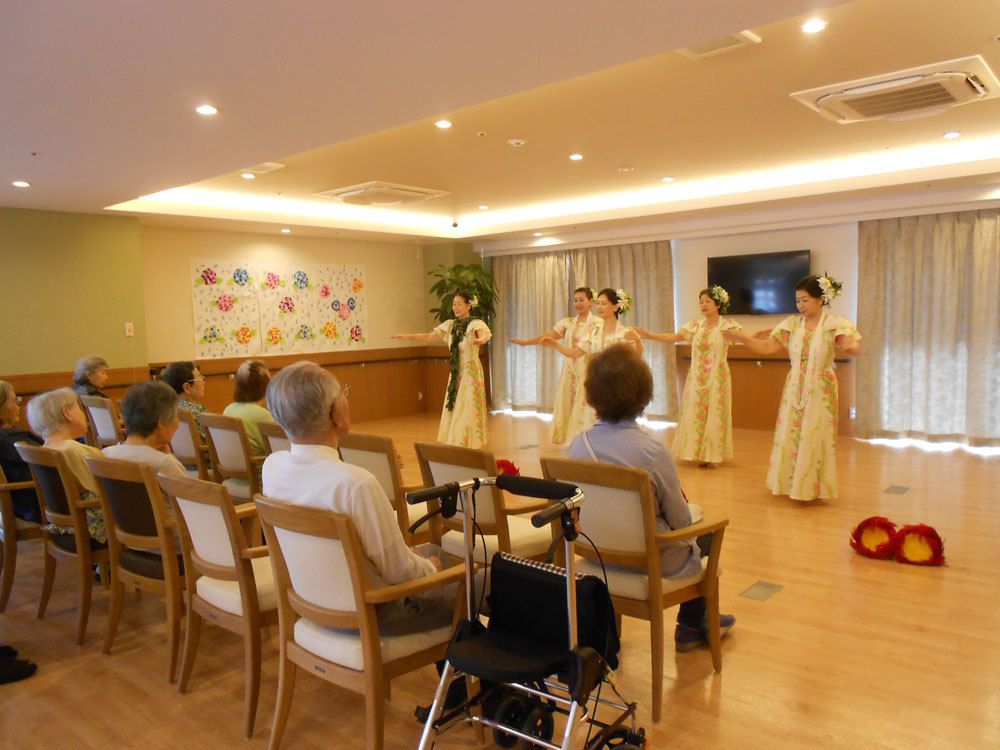 ５人の女性の踊るフラダンスを椅子に座って眺める入居者たち