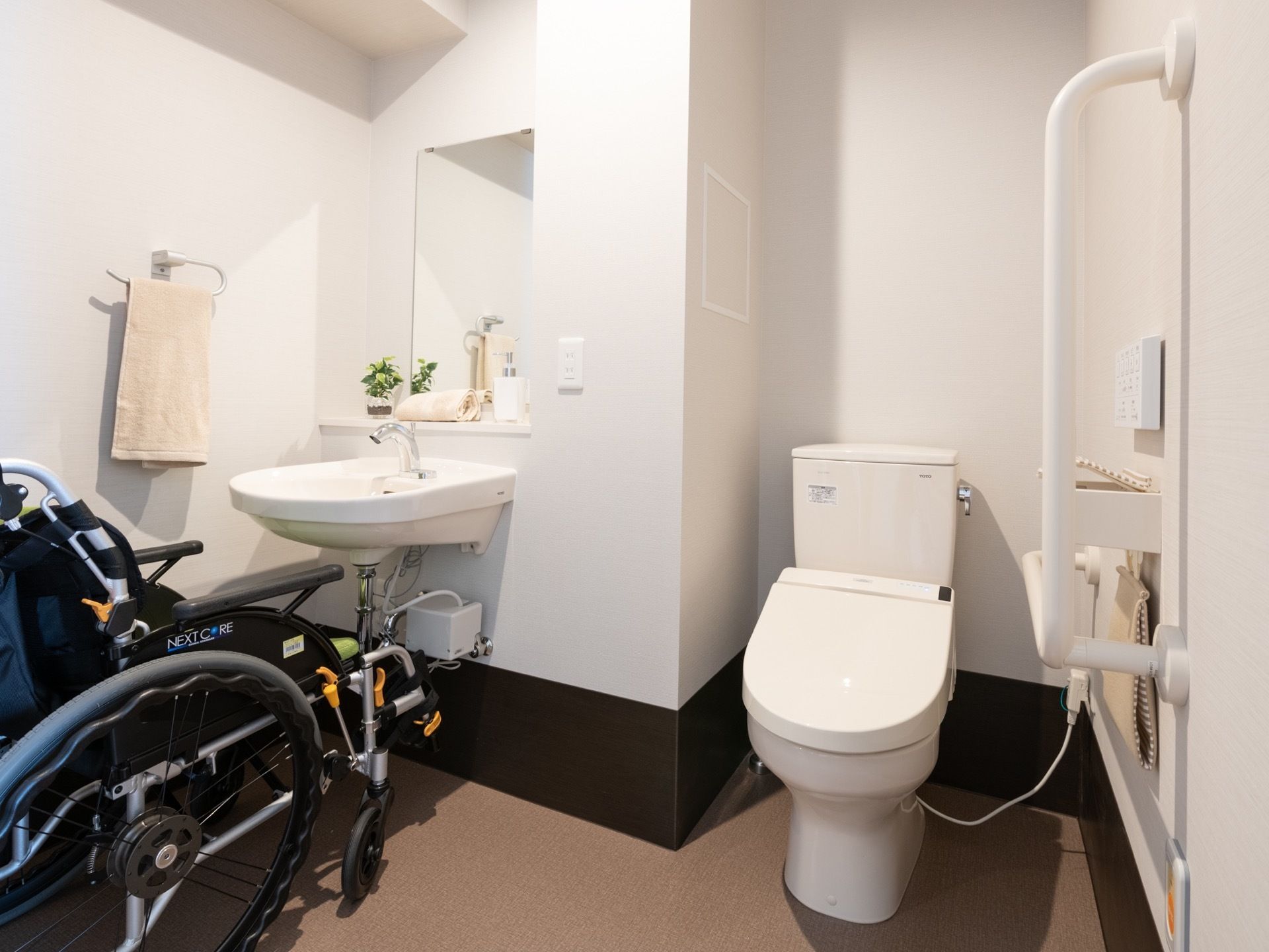 スペースを広く確保されたトイレに車椅子が置かれている。手すりが設置されているので、車椅子からスムーズに移動できる。