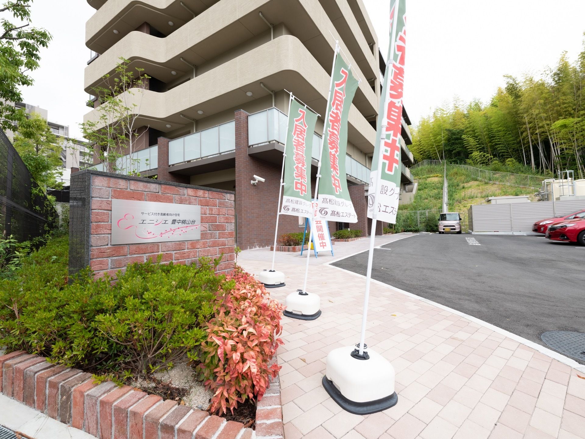 施設はベージュや茶色を基調とした、落ち着きのある高層の建物である。建物の手前には施設の目的と名称が記されたタイルが設置されている。