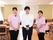清潔な装いに身を包んだ施設のスタッフたちが並んで写っている。背後では、食堂における入居者様やスタッフのにぎやかな光景が繰り広げられている。