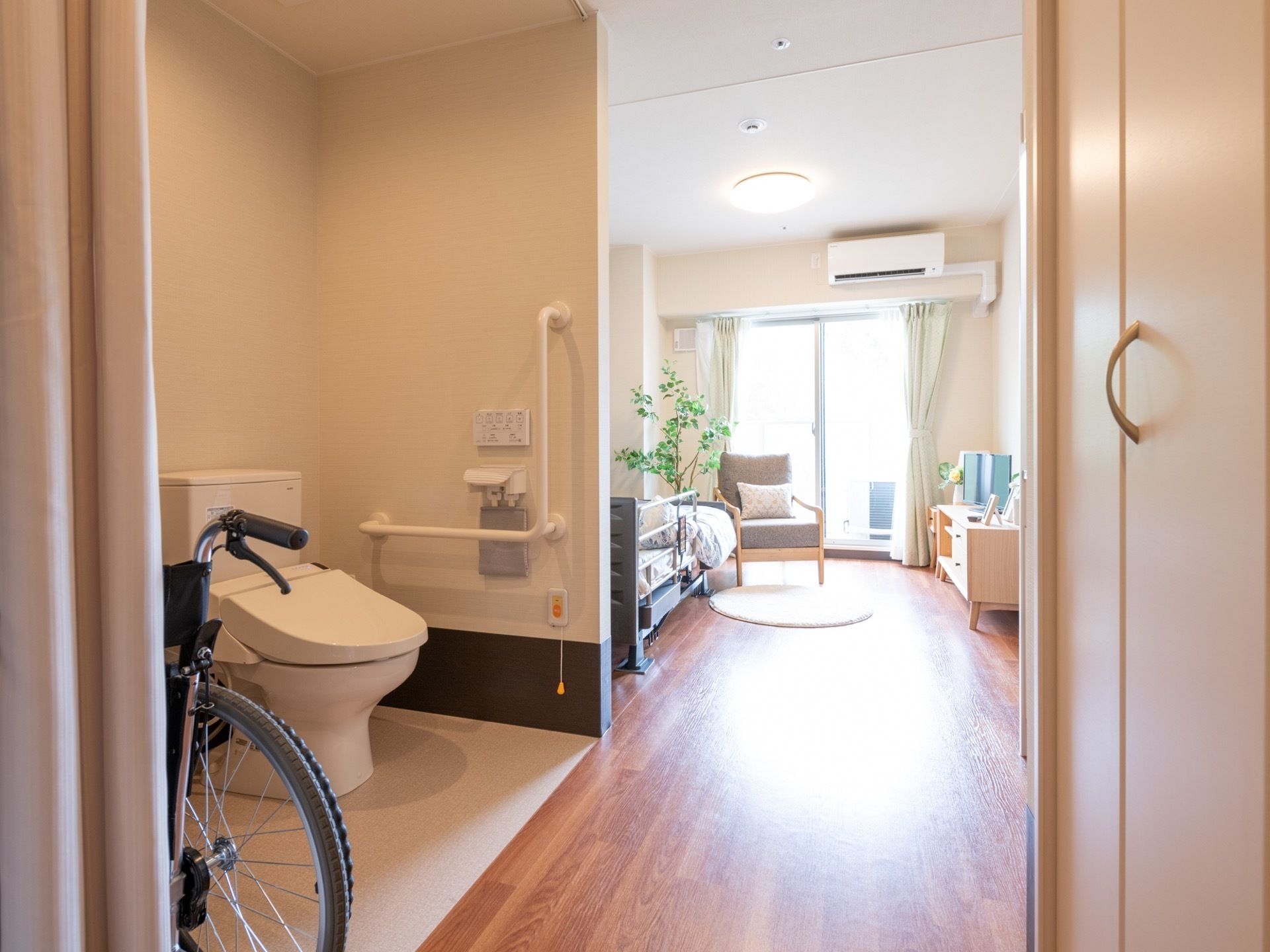 入口近くにトイレを配置した居室である。床面にはフローリングが敷かれており、室内奥の大きな窓からの自然光を明るく反射している。