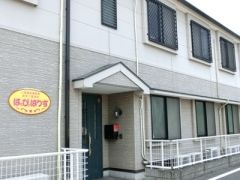 道路に面した1階部分に柵がある、2階建ての白とグレーのホーム