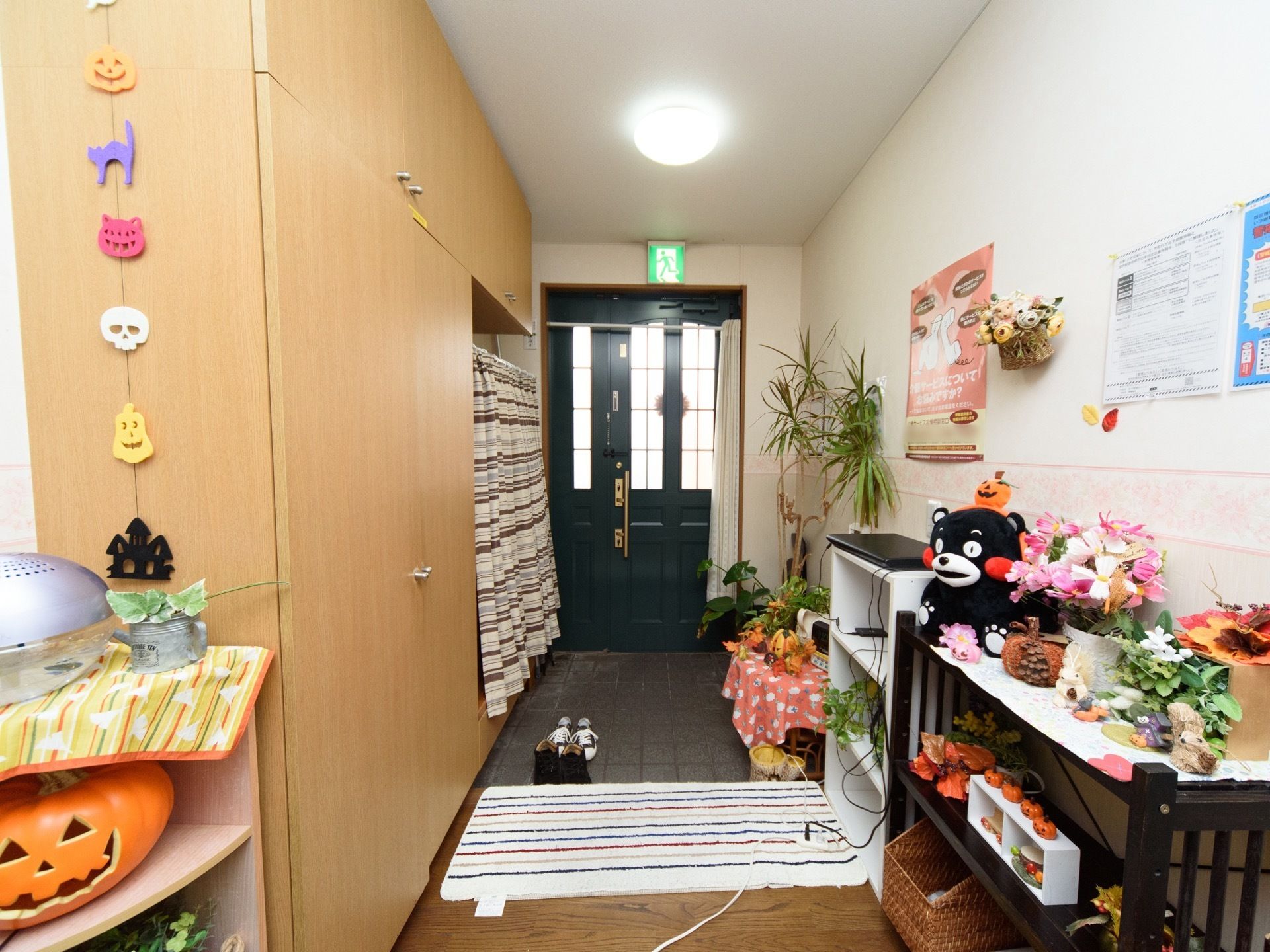 黒い扉の玄関があり、鉢植えの観葉植物や花がたくさん飾られている。木製の大きな下駄箱が備え付けられている。