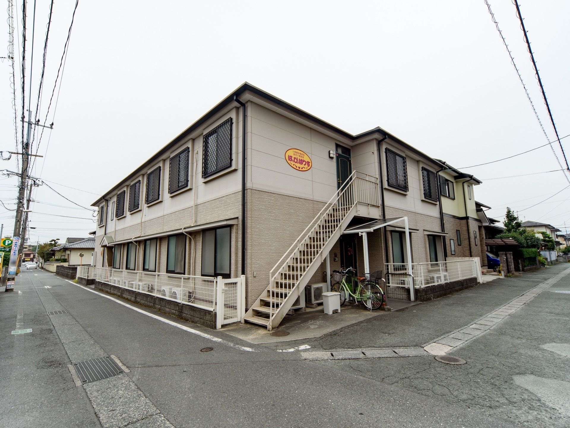 住宅街の一角に、２階建てのアパートが建っている。道路から玄関までは段差がなく、２階からは非常用の外階段が伸びている。